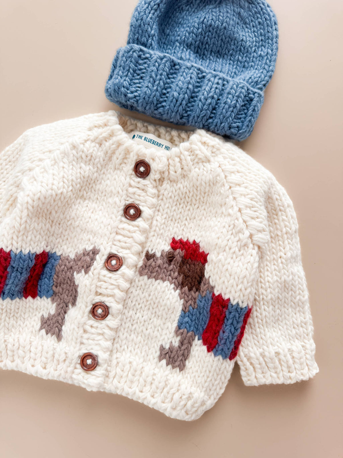The Blueberry Hill Cream Dachshund Cardigan and blue hat flat lay