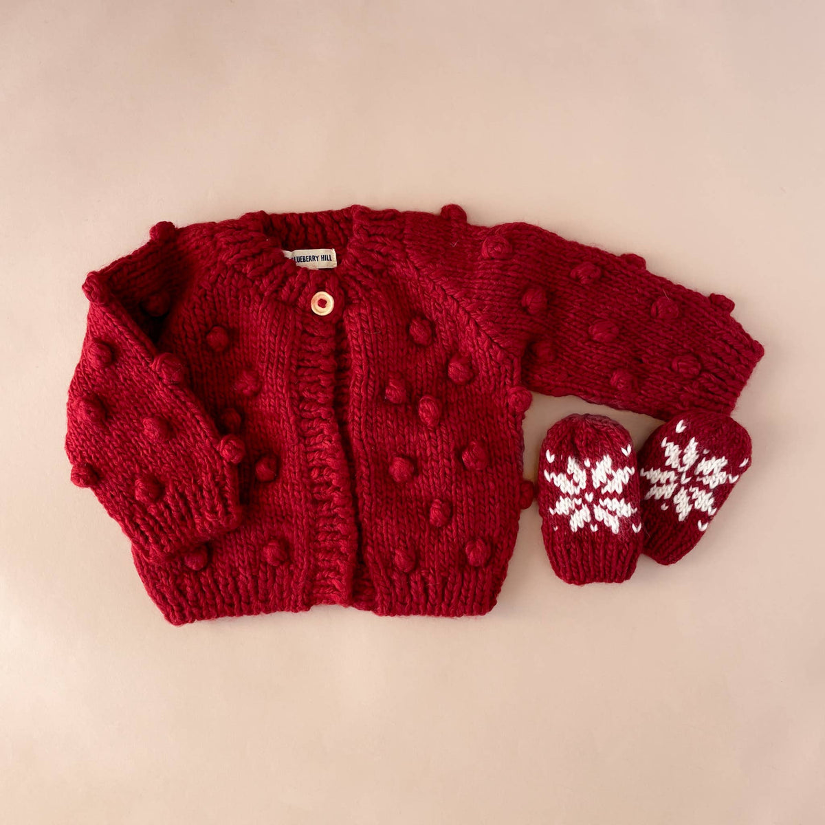 The Blueberry Hill Red Popcorn Cardigan flat lay with a red and cream hat
