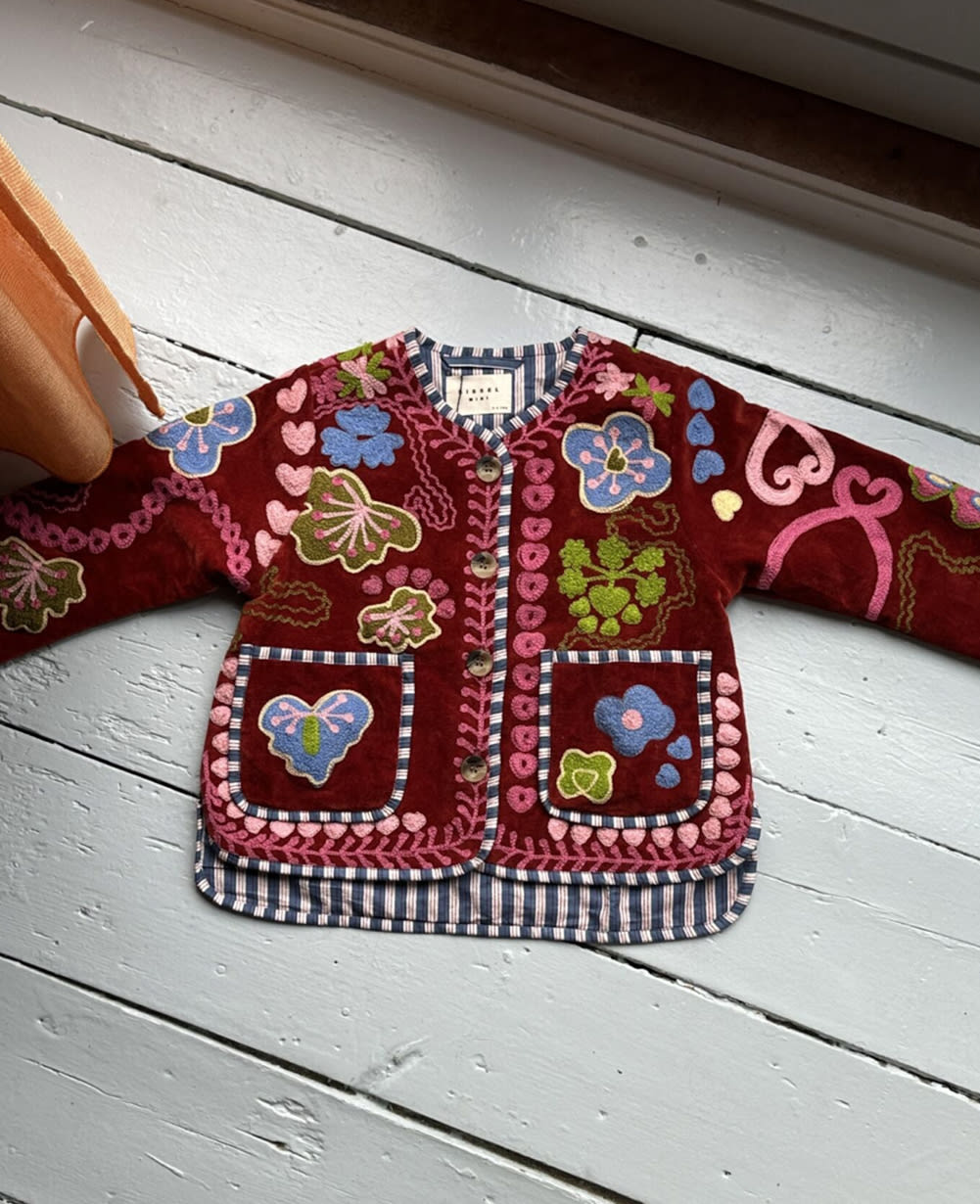 Sissel Edelbo front of the burgundy embroidered jacket hanging on a wall