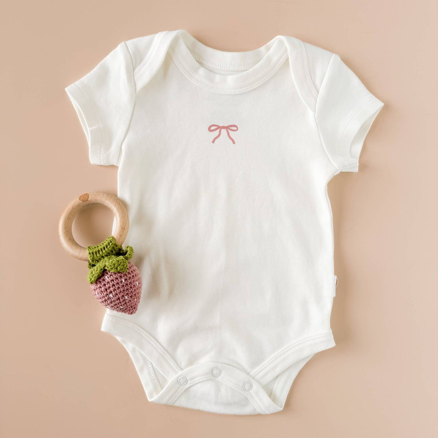 The Blueberry Hill strawberry crochet teether with white baby onesie
